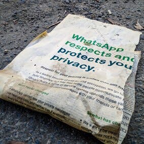 A torn, dirty newspaper clipping lying on the ground. Headline reads: "WhatsApp respects and protects you privacy."
