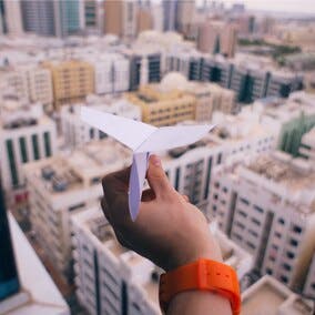 Image of a person holding a paper airplane about to throw it above a city.