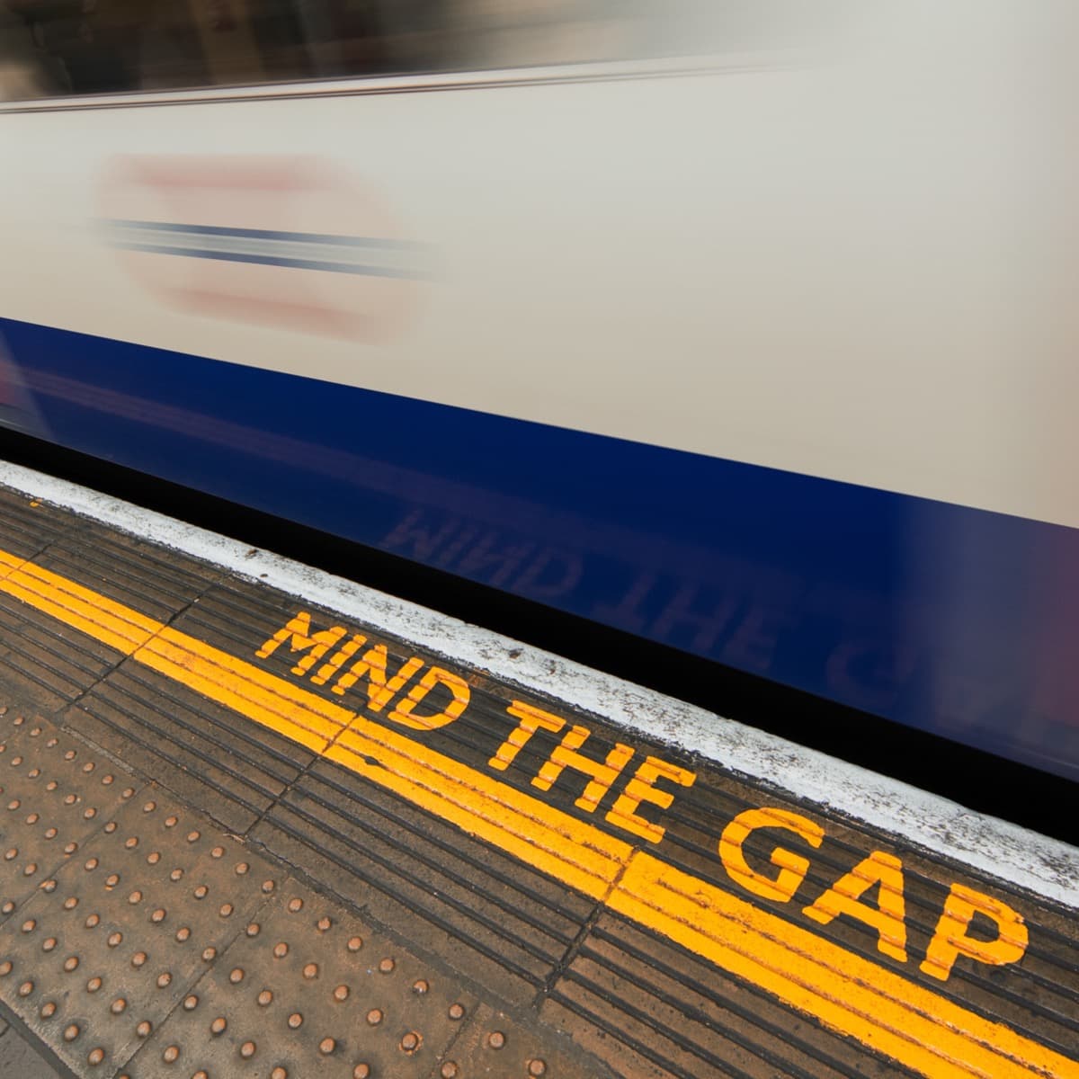 Image of a train going by a platform that says "Mind the Gap" on it.