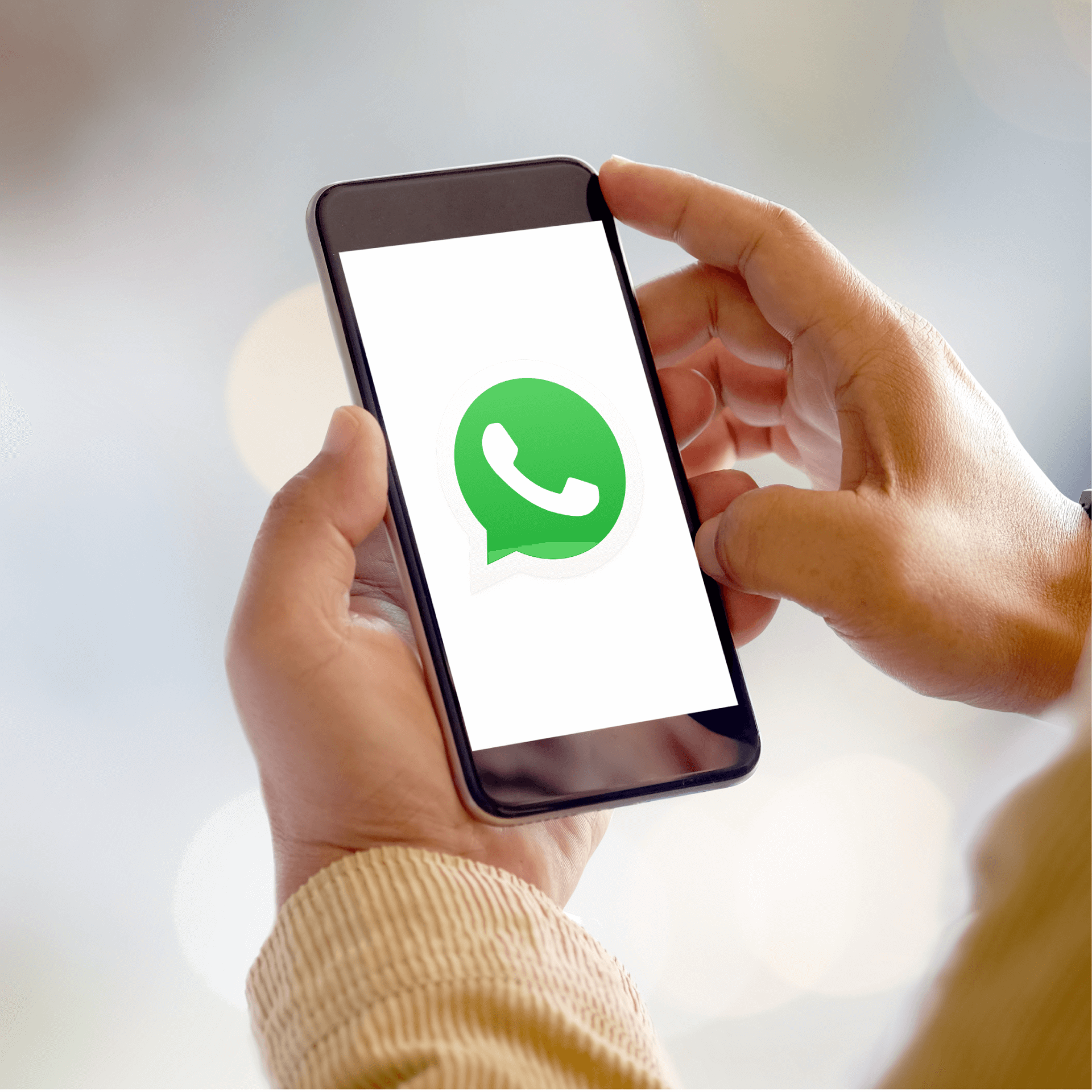 Image of a person holding a smartphone with the WhatsApp logo on the screen,